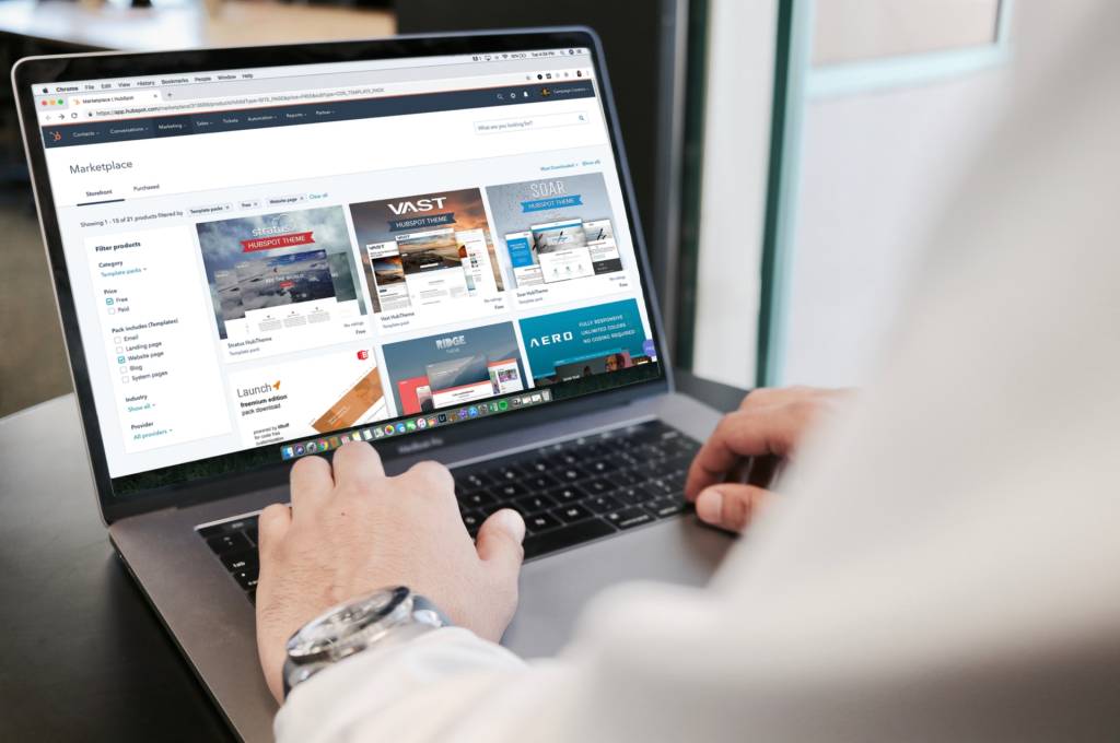 Man wearing watch typing on a laptop while browsing a marketplace website design optimized for a laptop.